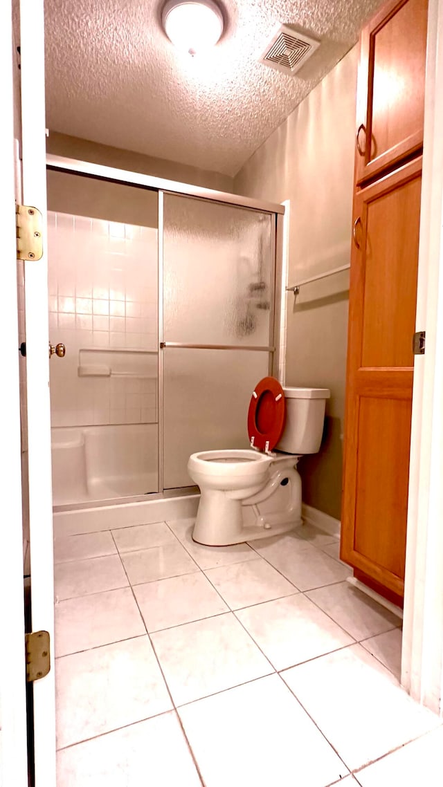 bathroom with a textured ceiling, toilet, a shower with door, and tile patterned floors