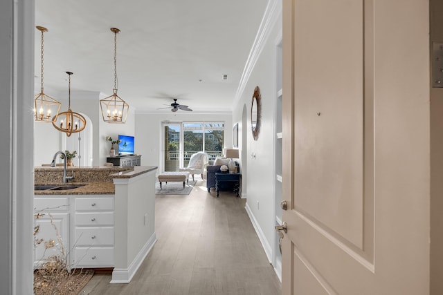 kitchen with sink, white cabinets, dark stone counters, hanging light fixtures, and crown molding