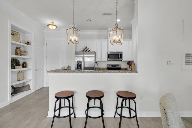 kitchen with hanging light fixtures, dark stone counters, kitchen peninsula, stainless steel appliances, and white cabinets