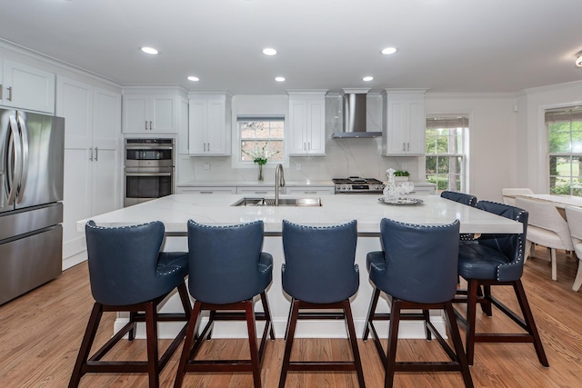 kitchen with wall chimney exhaust hood, stainless steel appliances, white cabinets, a sink, and crown molding