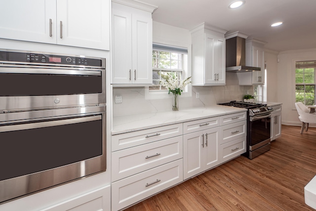 kitchen featuring recessed lighting, wall chimney range hood, light wood-style floors, appliances with stainless steel finishes, and white cabinetry