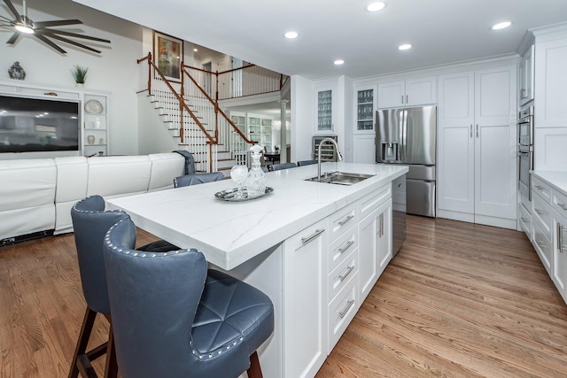 kitchen with white cabinets, stainless steel fridge with ice dispenser, a sink, a center island with sink, and open floor plan