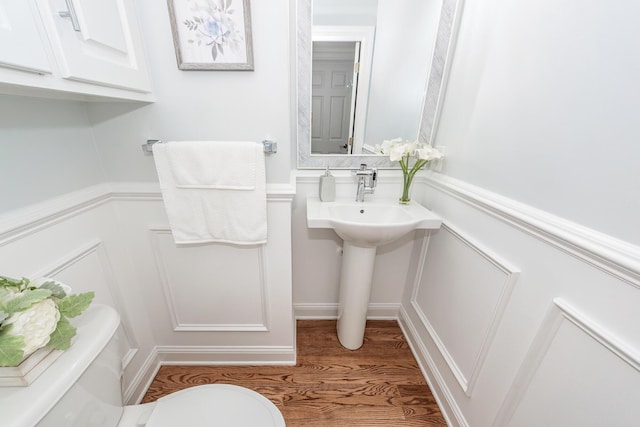 bathroom featuring wainscoting, toilet, wood finished floors, and a decorative wall