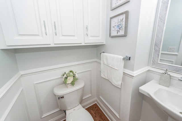 bathroom with a decorative wall, toilet, and wainscoting
