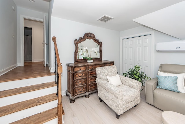 sitting room with baseboards, light wood-style flooring, visible vents, and an AC wall unit