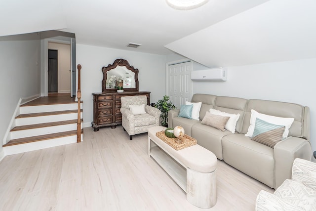 living area featuring a wall mounted air conditioner, stairs, light wood-type flooring, baseboards, and visible vents