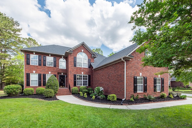 colonial house featuring brick siding, a shingled roof, and a front lawn