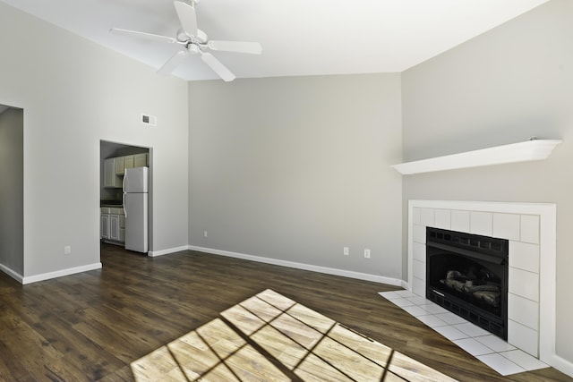 unfurnished living room featuring dark hardwood / wood-style floors, high vaulted ceiling, ceiling fan, and a tiled fireplace