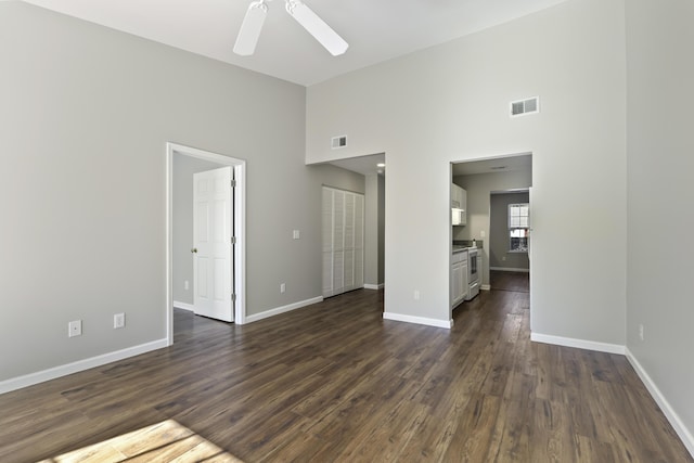 unfurnished living room featuring a towering ceiling, ceiling fan, and dark wood-type flooring