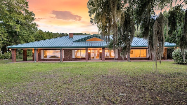 1085 Harts Bluff Rd, Wadmalaw Island, SC 29487 - back of house at dusk with a standing seam roof, a lawn, a metal roof, and a chimney