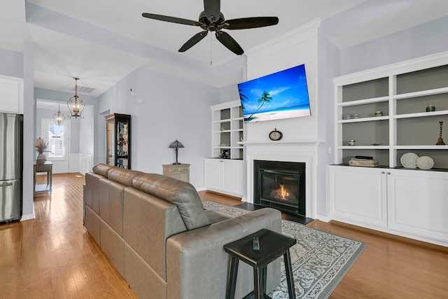 living area with wood finished floors, visible vents, wainscoting, a glass covered fireplace, and ceiling fan with notable chandelier