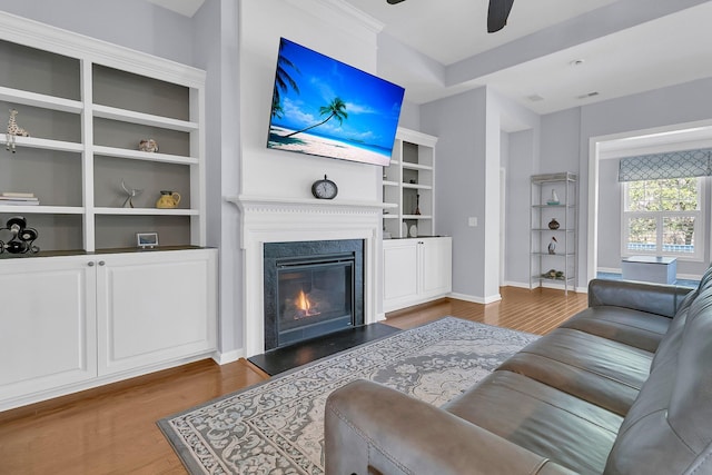 living area with a glass covered fireplace, wood finished floors, baseboards, and ceiling fan