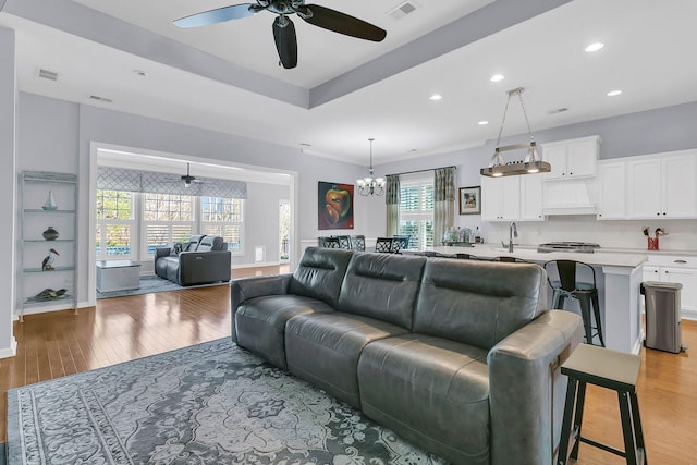 living room with ceiling fan with notable chandelier, visible vents, and light wood-style floors
