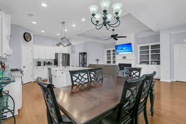 dining space featuring a fireplace, light wood-style flooring, recessed lighting, and ceiling fan with notable chandelier