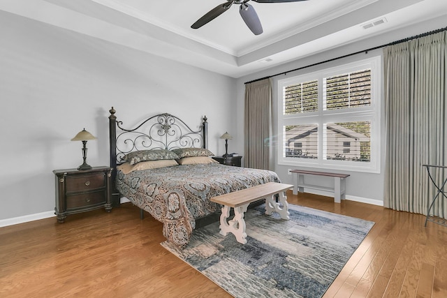 bedroom with a raised ceiling, wood finished floors, visible vents, ornamental molding, and baseboards