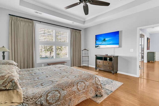 bedroom with baseboards, visible vents, wood finished floors, crown molding, and a raised ceiling