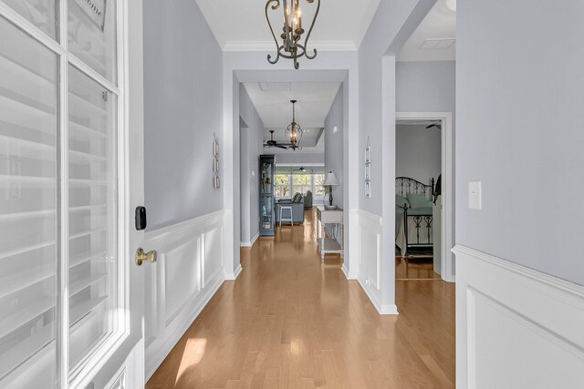 entrance foyer with crown molding, wood finished floors, a wainscoted wall, and a notable chandelier