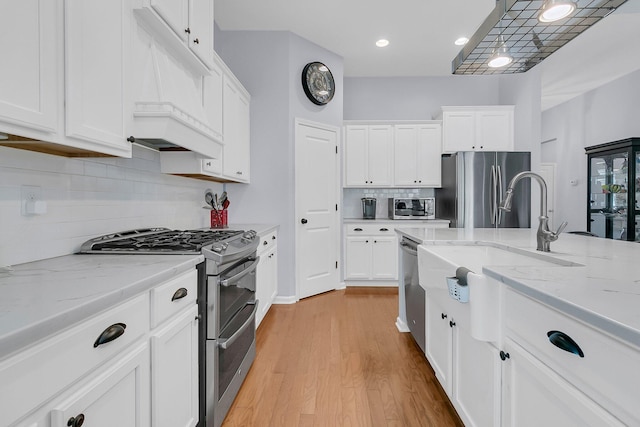 kitchen featuring white cabinets, stainless steel appliances, light wood-style floors, decorative backsplash, and light stone counters