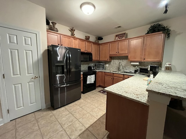 kitchen featuring kitchen peninsula, backsplash, light stone counters, sink, and black appliances