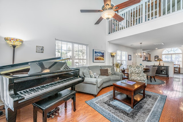 living room with ceiling fan with notable chandelier, a high ceiling, and hardwood / wood-style floors