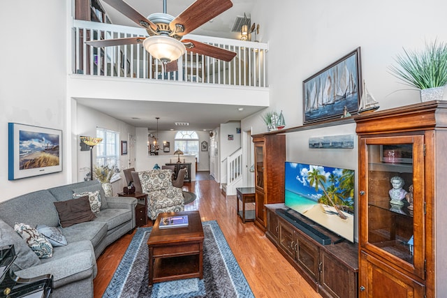 living room featuring wood-type flooring, ceiling fan with notable chandelier, and a high ceiling