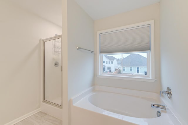 bathroom with a shower stall, a bath, and baseboards