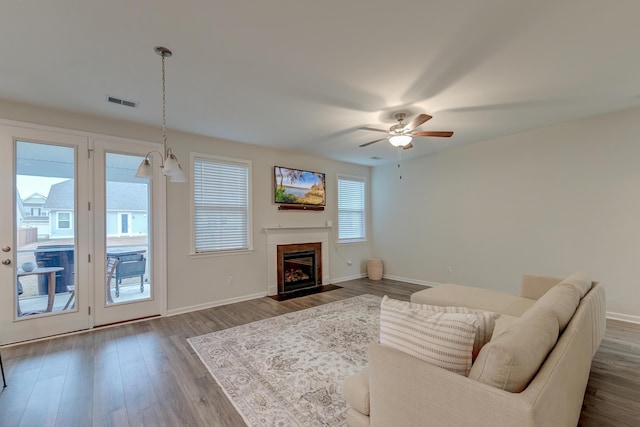 living area featuring ceiling fan with notable chandelier, dark wood-style flooring, a fireplace with flush hearth, visible vents, and baseboards