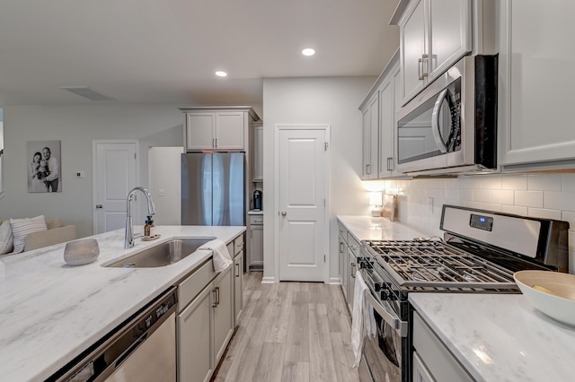 kitchen with a sink, appliances with stainless steel finishes, light stone countertops, light wood finished floors, and tasteful backsplash