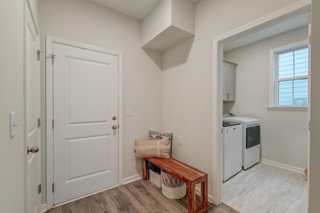 clothes washing area with light wood-type flooring, washing machine and clothes dryer, cabinet space, and baseboards