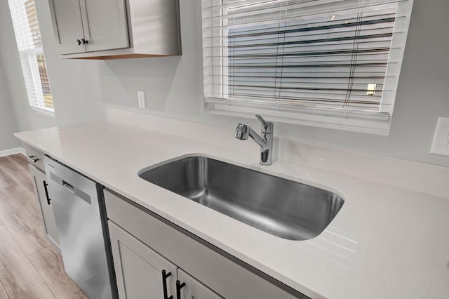 kitchen with dishwasher, gray cabinets, light wood-type flooring, and sink