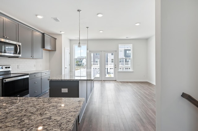 kitchen with appliances with stainless steel finishes, dark hardwood / wood-style flooring, light stone counters, pendant lighting, and a kitchen island