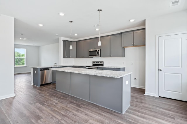 kitchen with gray cabinetry, hanging light fixtures, light stone countertops, a kitchen island, and stainless steel appliances