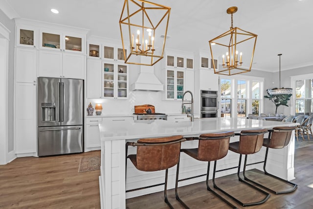 kitchen with sink, an inviting chandelier, appliances with stainless steel finishes, an island with sink, and custom range hood