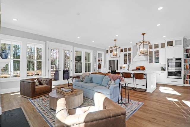 living room with ornamental molding, an inviting chandelier, light hardwood / wood-style floors, and french doors