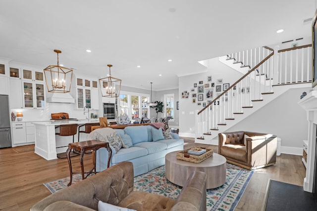 living room featuring crown molding, sink, an inviting chandelier, and light hardwood / wood-style floors