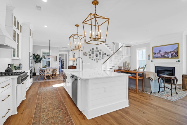 kitchen with white cabinets, hanging light fixtures, light hardwood / wood-style floors, stainless steel appliances, and a center island with sink