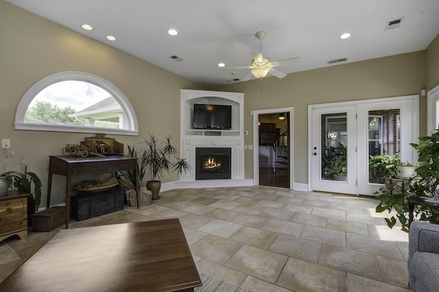living area with a warm lit fireplace, visible vents, lofted ceiling, and a ceiling fan