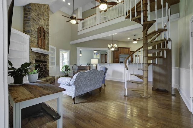 living area featuring stairway, ceiling fan with notable chandelier, a towering ceiling, a stone fireplace, and wood finished floors
