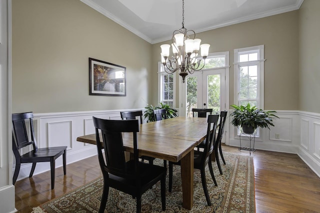 dining space with a wainscoted wall, a notable chandelier, dark wood finished floors, a decorative wall, and ornamental molding