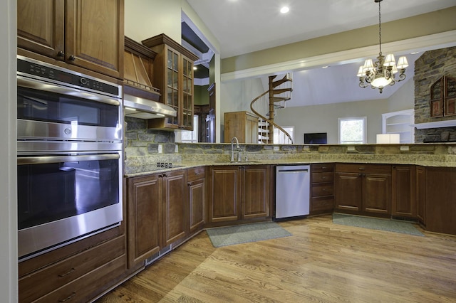 kitchen with tasteful backsplash, hanging light fixtures, a sink, light wood-style floors, and appliances with stainless steel finishes