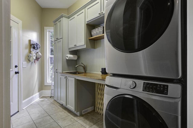 laundry room with visible vents, stacked washer / drying machine, a sink, cabinet space, and light tile patterned floors