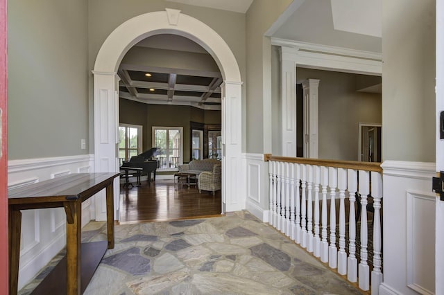 hall with coffered ceiling, a wainscoted wall, beam ceiling, a decorative wall, and ornate columns
