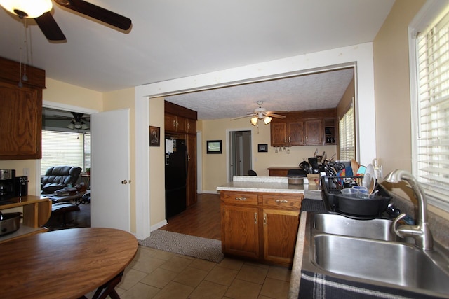 kitchen featuring brown cabinetry, freestanding refrigerator, a sink, ceiling fan, and a peninsula