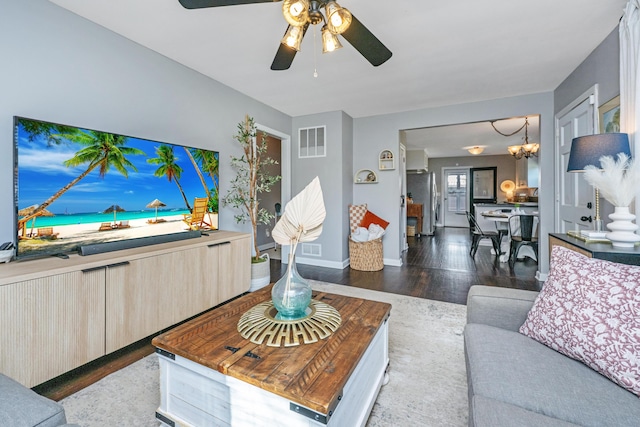 living area featuring ceiling fan with notable chandelier, visible vents, baseboards, and wood finished floors