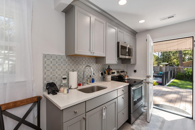 kitchen featuring backsplash, appliances with stainless steel finishes, light wood-type flooring, gray cabinets, and sink