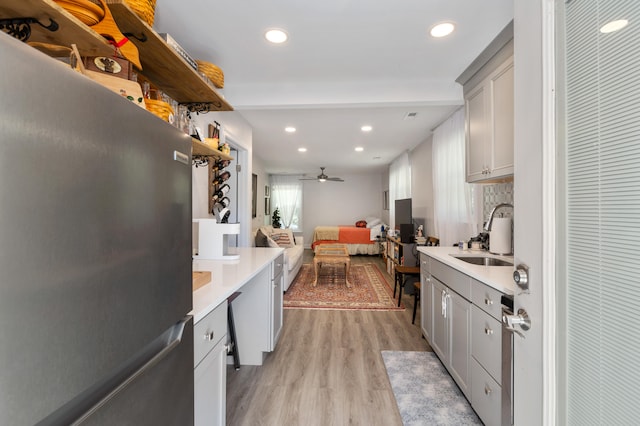 kitchen featuring stainless steel refrigerator, backsplash, sink, light hardwood / wood-style floors, and ceiling fan