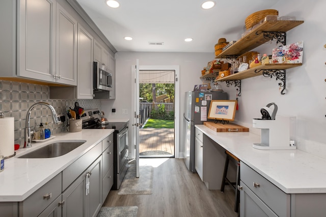 kitchen with light stone countertops, sink, stainless steel appliances, gray cabinets, and light hardwood / wood-style flooring