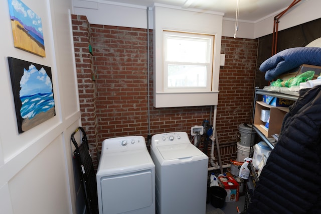 laundry area with crown molding, washer and dryer, and brick wall