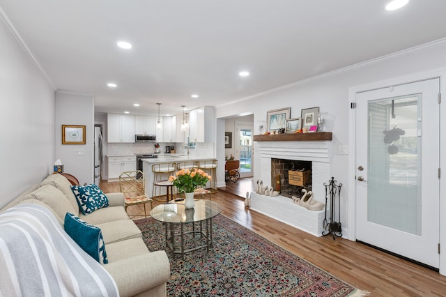 living room featuring sink, ornamental molding, light hardwood / wood-style flooring, and a brick fireplace