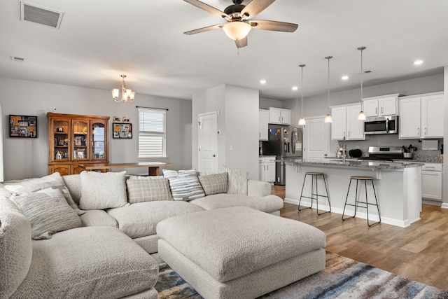 living room with ceiling fan with notable chandelier and hardwood / wood-style floors